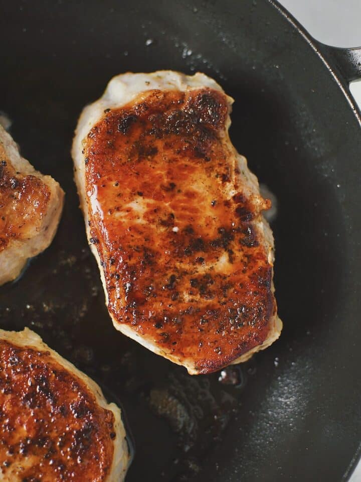 Olive oil warmed in a skillet, and searing the sous vide pork chops until crisp and dark brown on both sides.