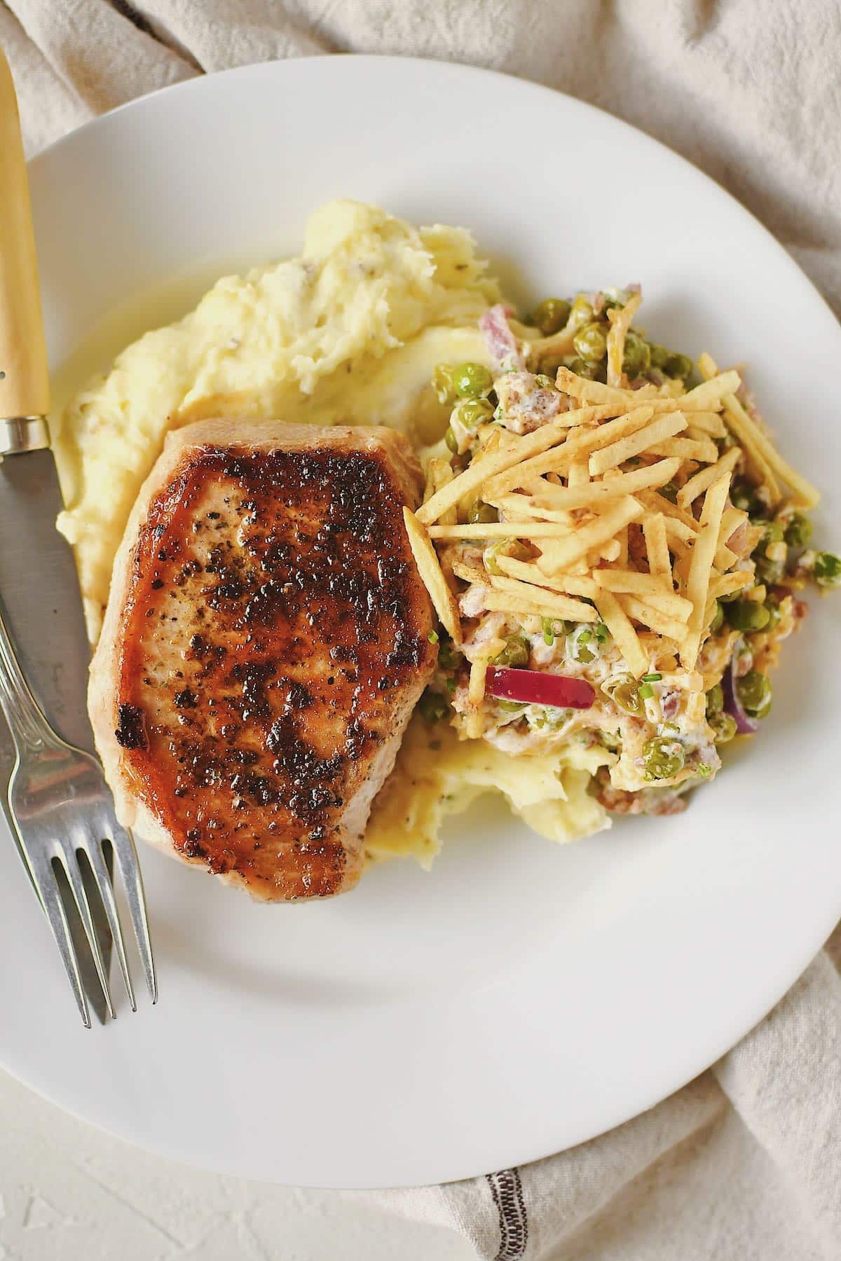Sous Vide Pork Chop served on a plate with mashed potatoes and pea salad.