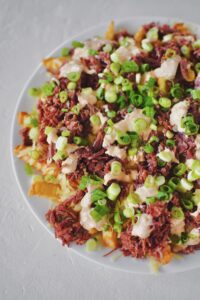 Finished Irish Nachos with white cheddar, corned beef, remoulade, and green onions on top of crispy crinkle french fries.