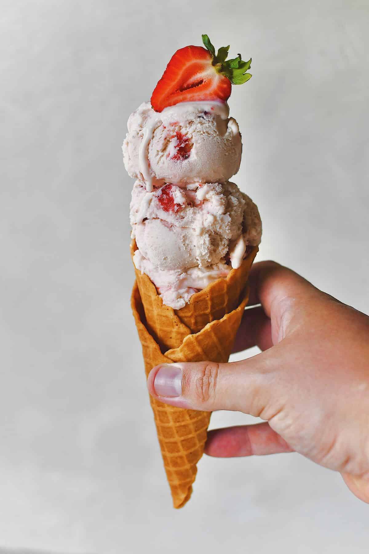 Strawberry Ice Cream served in a cone and being handed off.