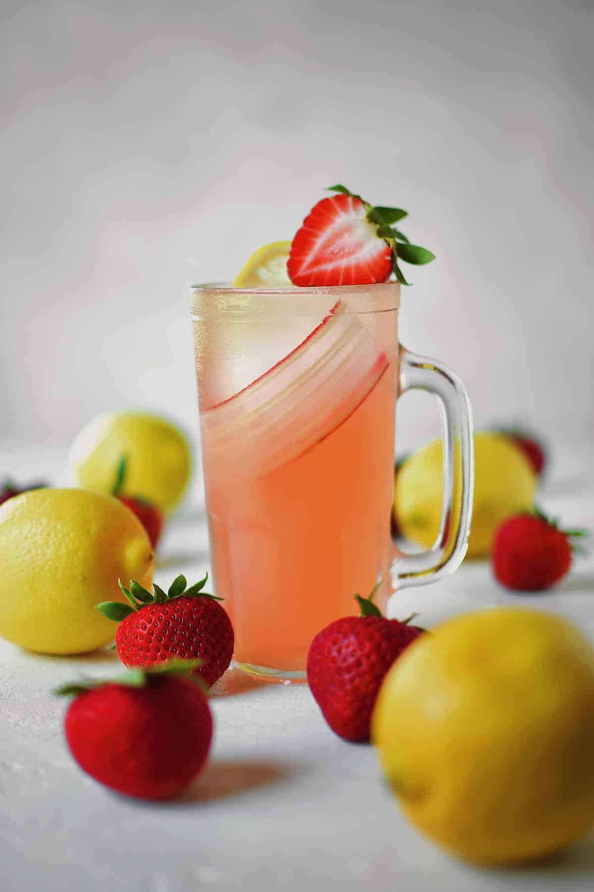 A glass of strawberry lemonade in a table with fresh strawberries and lemons around it.