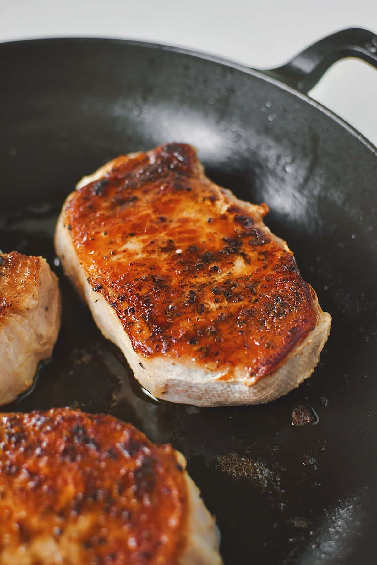 Olive oil warmed in a skillet, and searing the sous vide pork chops until crisp and dark brown on both sides.