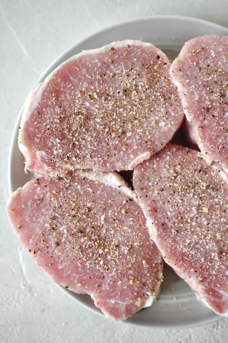 Pork Chops seasoned on both sides with salt and pepper and resting on a plate.