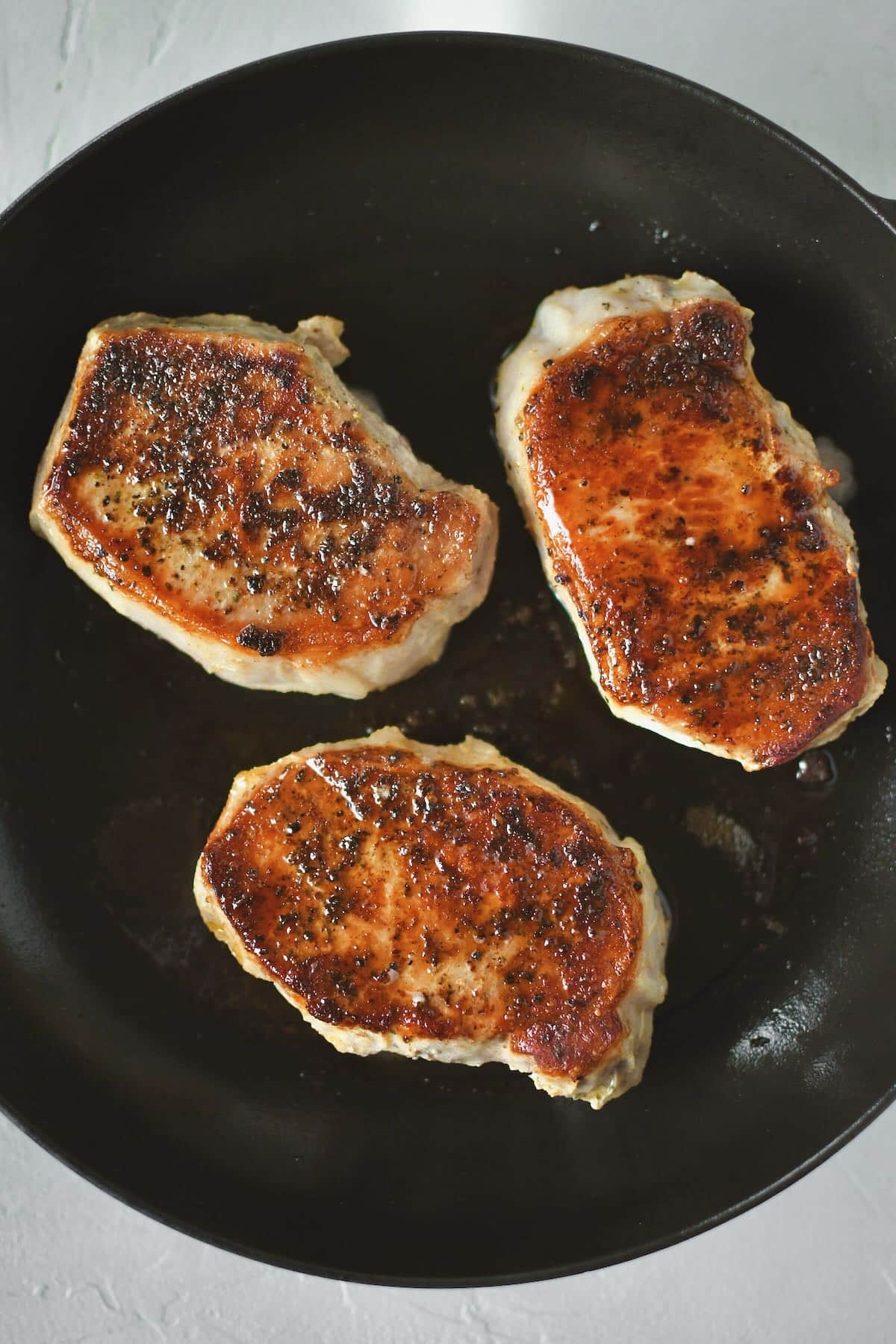 Olive oil warmed in a skillet, and searing the sous vide pork chops until crisp and dark brown on both sides.
