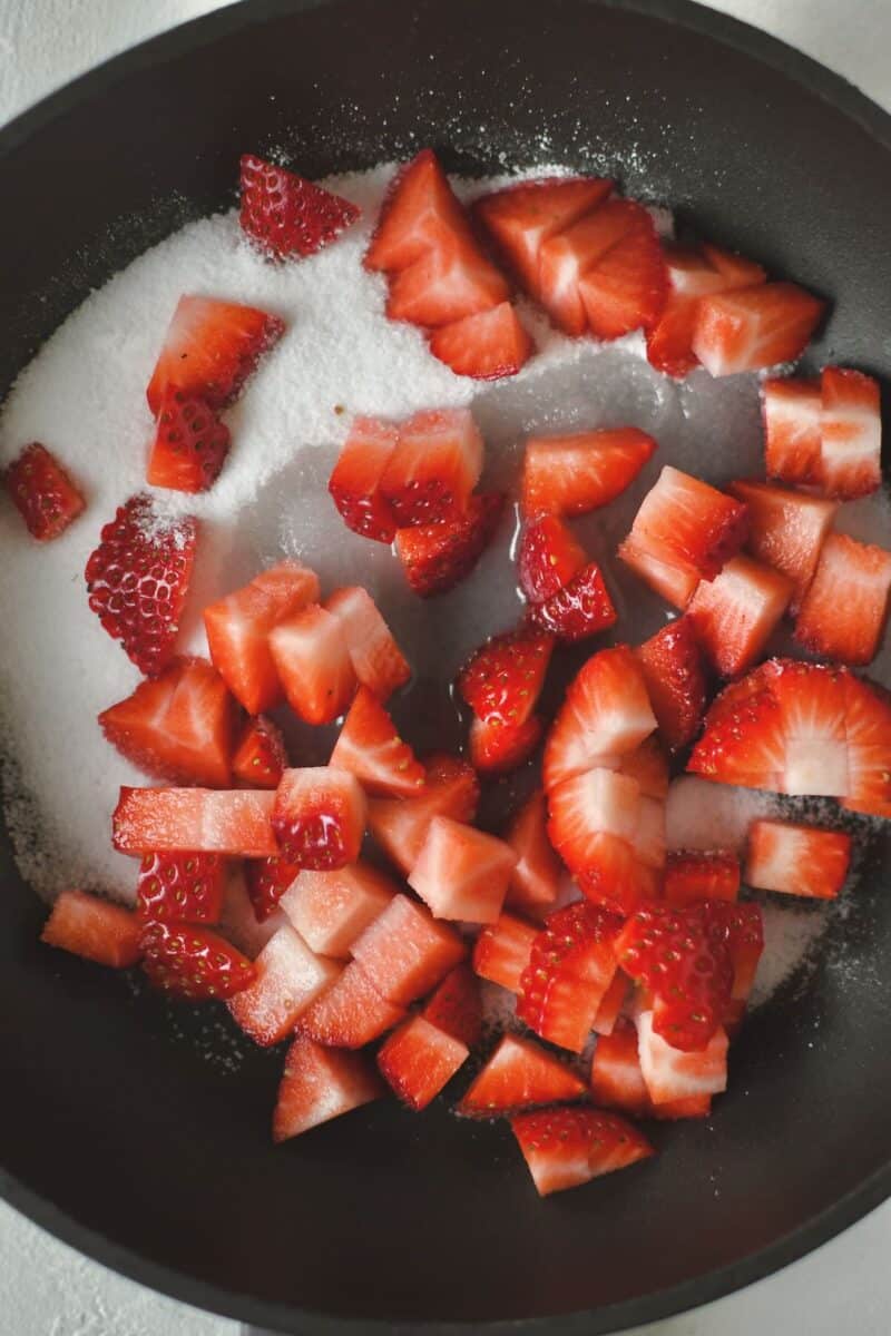 Strawberries and sugar added to a skillet with a splash of water to be cooked quickly.