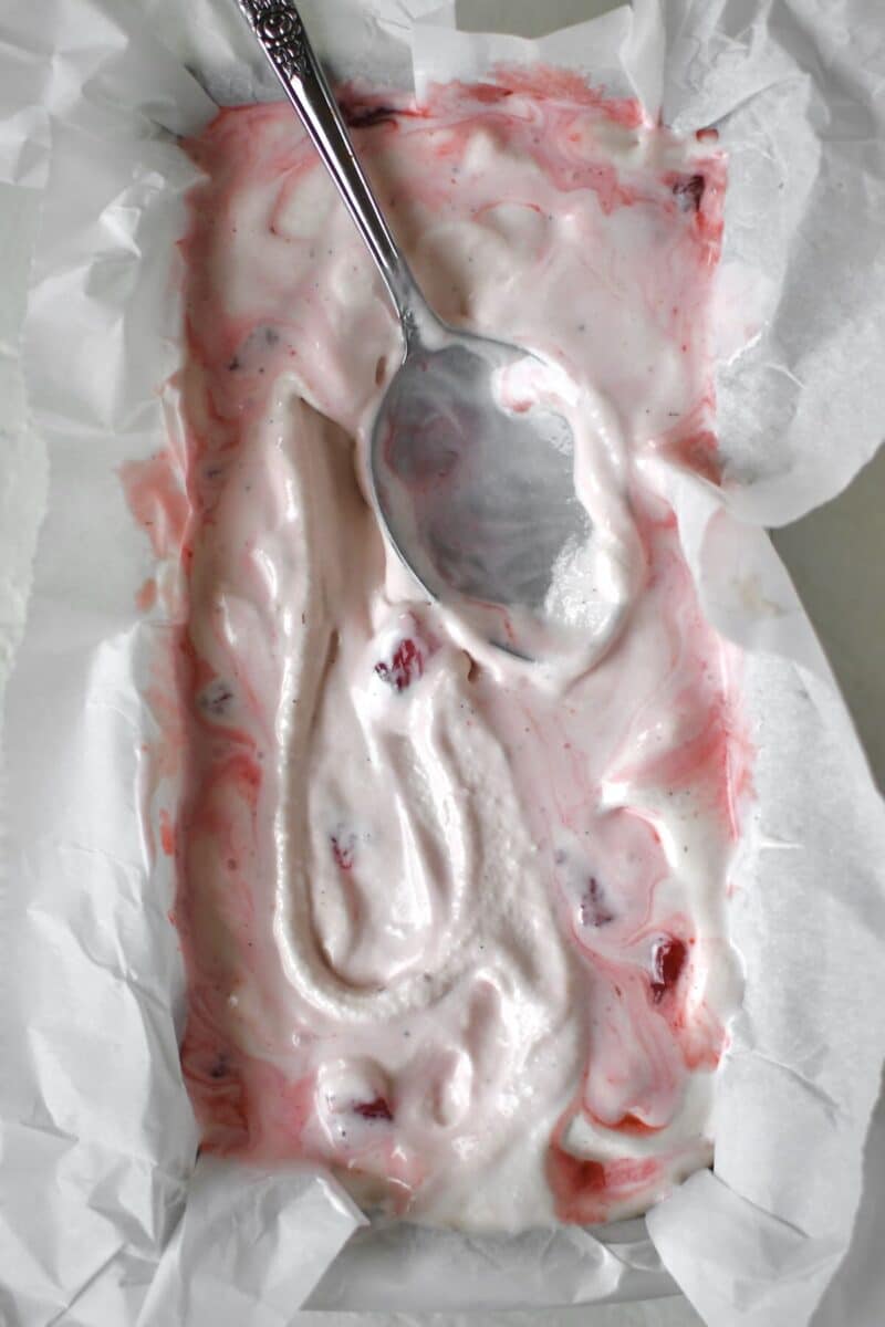 Mixing the cooked strawberries into the churned ice cream in a freezer safe storage dish.