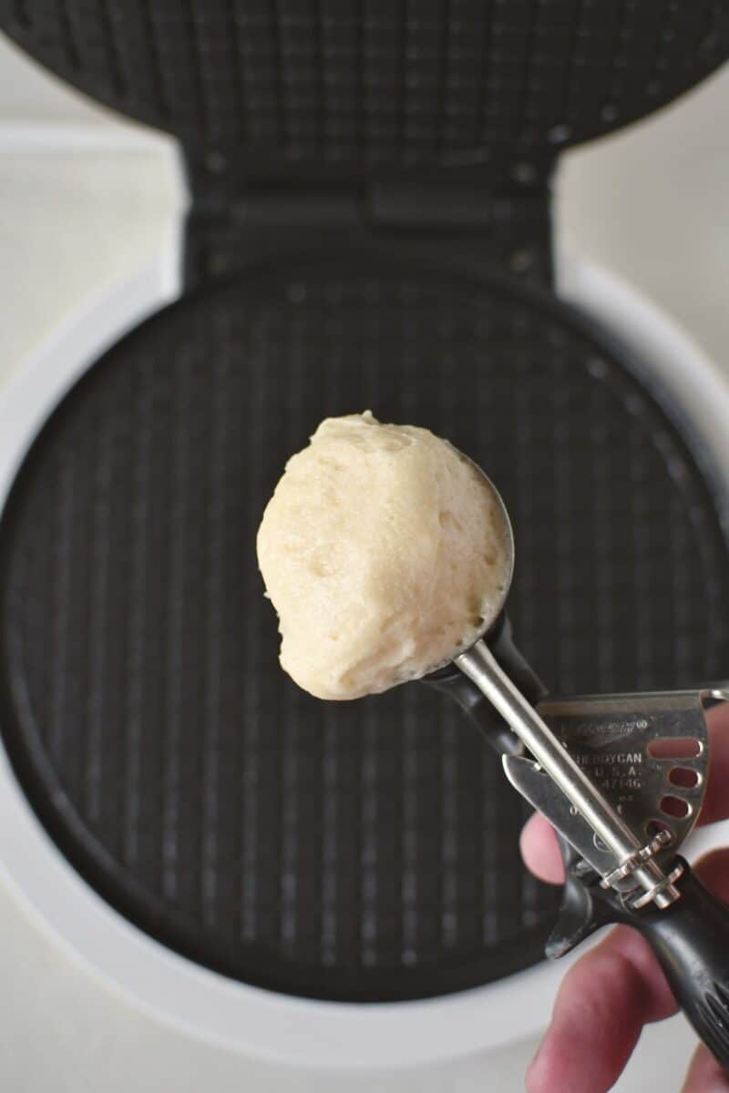 Scooping some batter and placing it on a waffle cone iron.