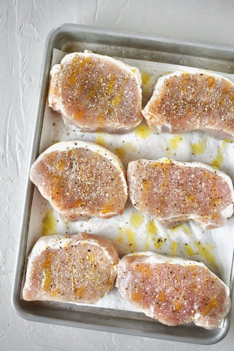 Pork chops that have been patted dry after removing from the brine. Coated with olive oil, salt, and pepper.