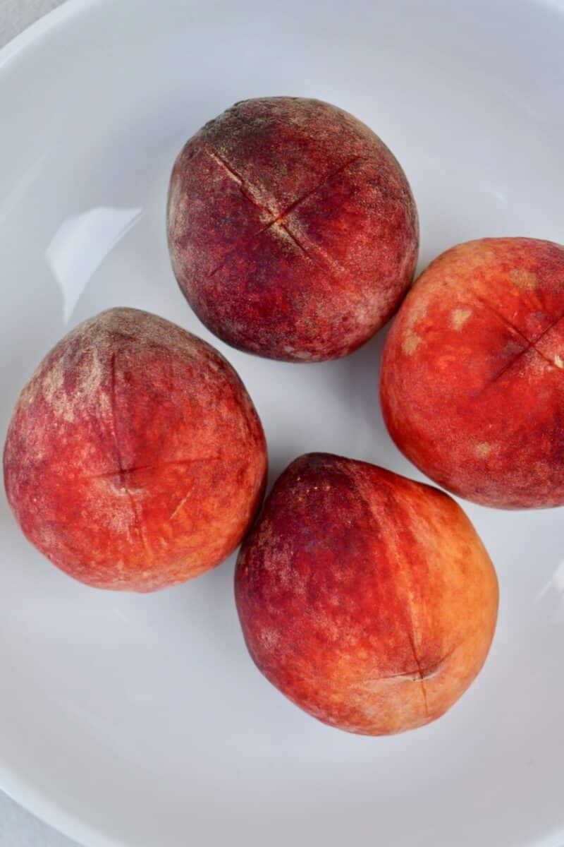 Whole peaches before blanching with an x scored into the bottom of each.