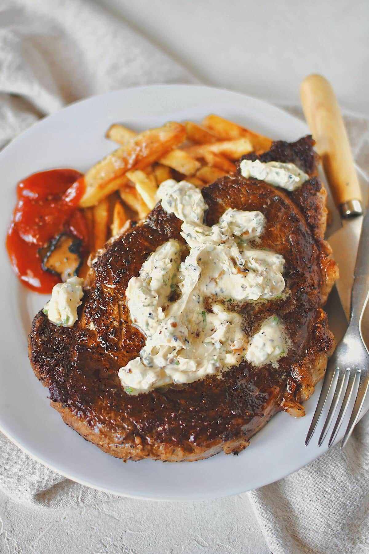 Steak Frites, on a plate, the steak topped with truffle butter and the frites served with truffle chili sauce.