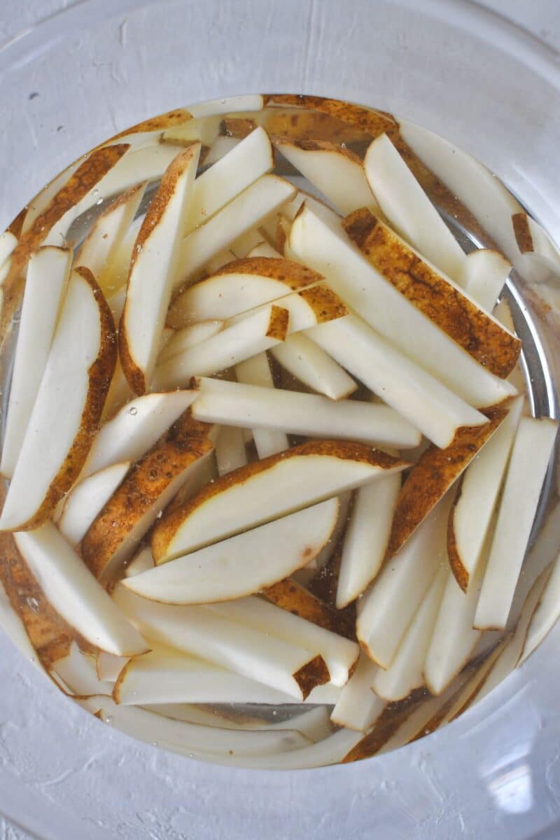 Russet potatoes, cut into fries, or frites in french, soaking in water after rinsing.