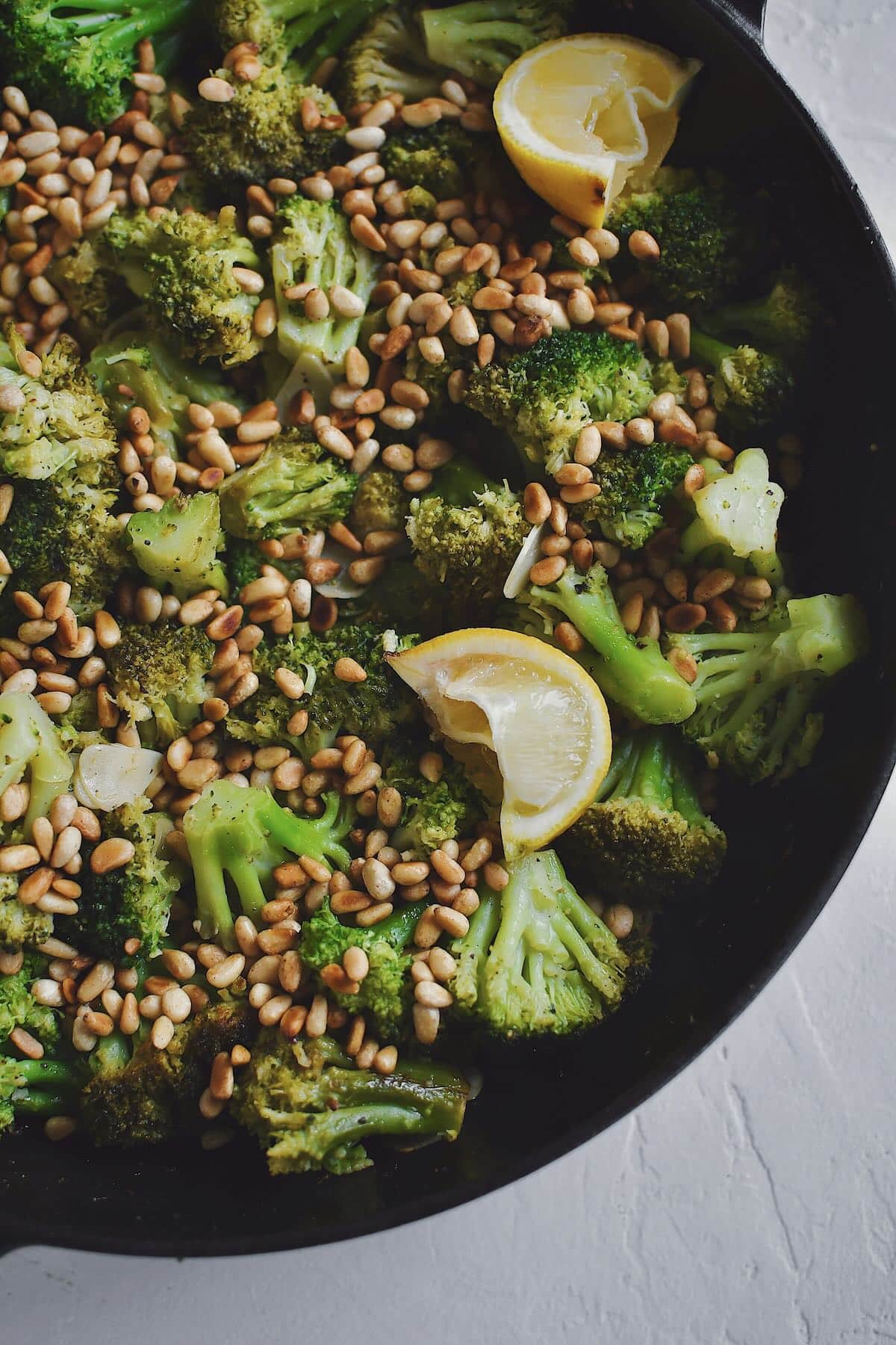 Sauteed Broccoli topped with toasted pine nuts and lemon wedges, ready to eat.