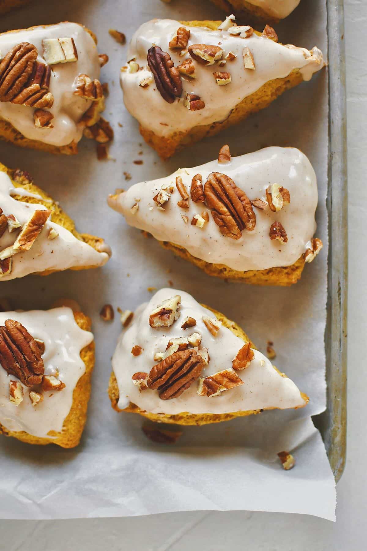 Pumpkin Scones, on a tray, topped with maple glaze and chopped pecans, ready to eat.