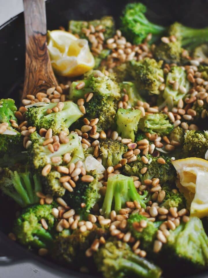 Sauteed Broccoli topped with toasted pine nuts and lemon wedges, ready to eat.