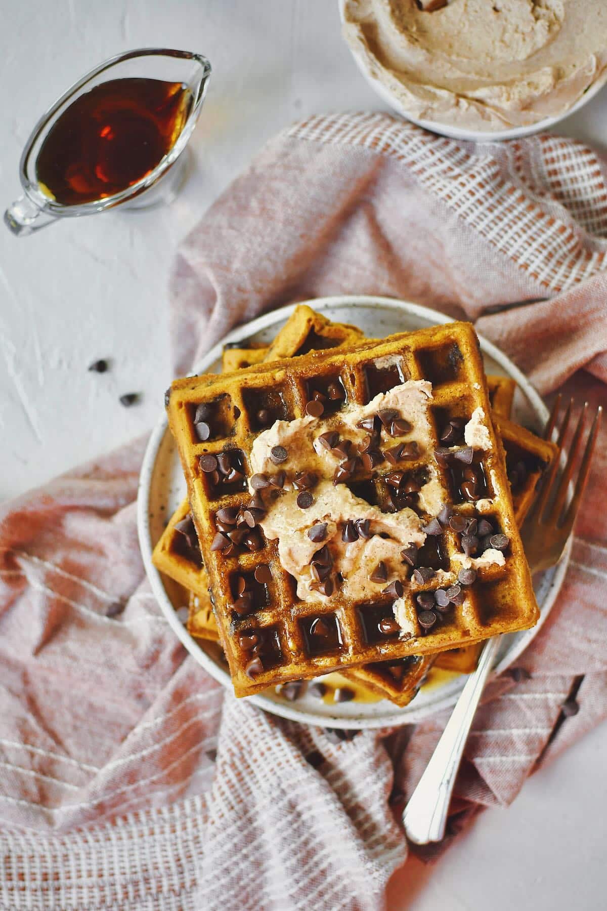 Pumpkin Waffles Recipe on a plate, topped with cinnamon butter, maple syrup, and chocolate chips.