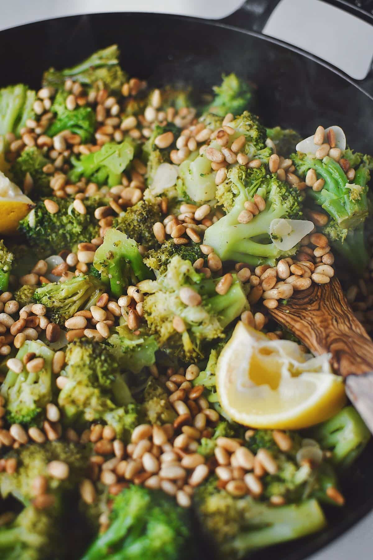 Sauteed Broccoli topped with toasted pine nuts and lemon wedges, ready to eat.