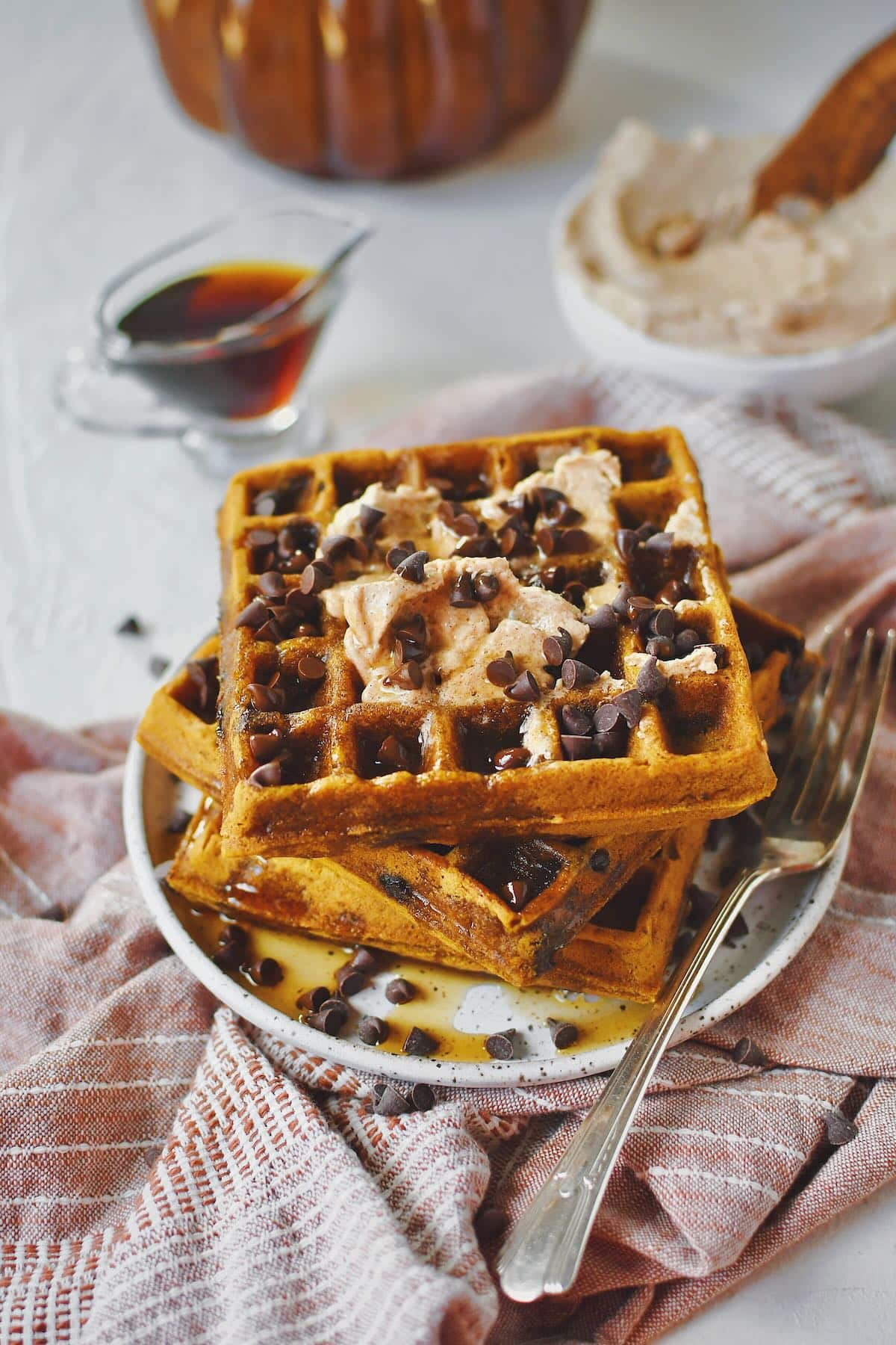 Pumpkin Waffles Recipe on a plate, topped with cinnamon butter, maple syrup, and chocolate chips.