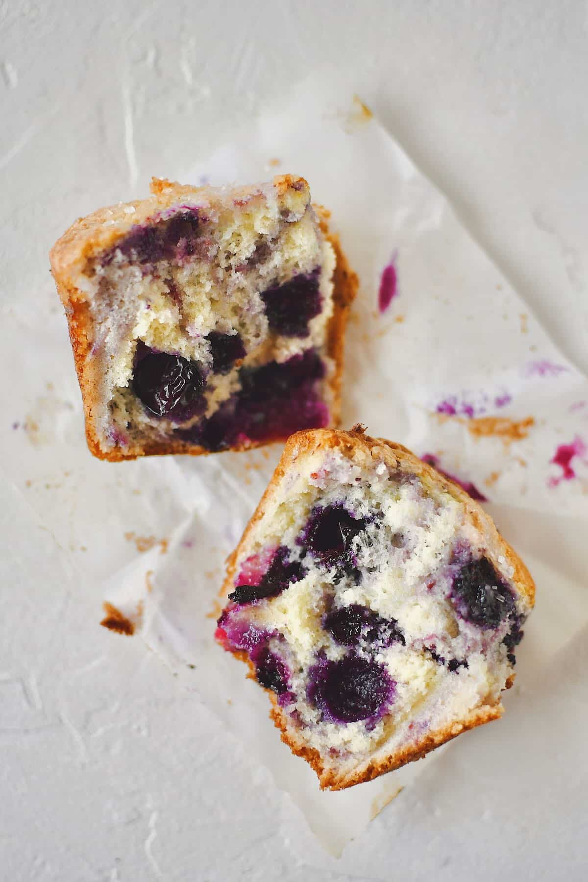 Easy Blueberry Muffins laid out on a table, with one of them having the wrapper removed.