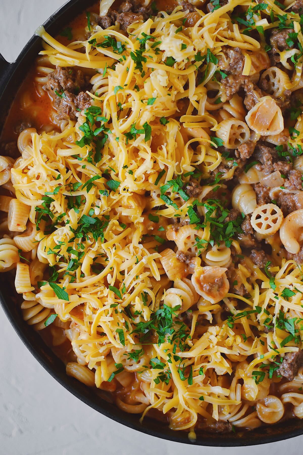 Finished Homemade Hamburger Helper in the pan, topped with cheddar cheese and parsley, ready to eat.