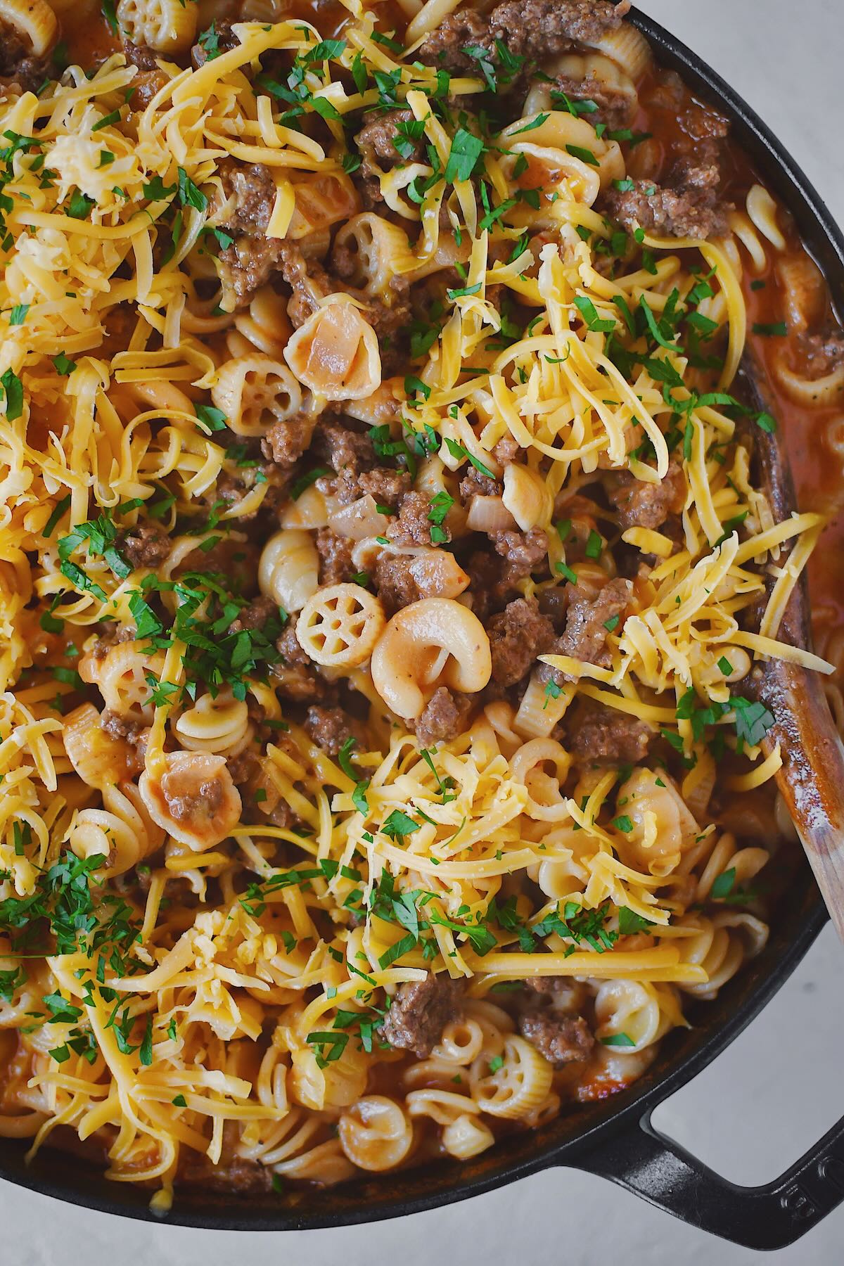 Finished Homemade Hamburger Helper in the pan, topped with cheddar cheese and parsley, ready to eat.