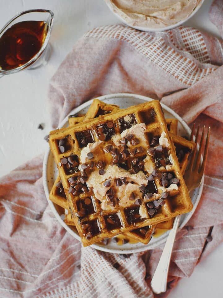 Pumpkin Waffles Recipe on a plate, topped with cinnamon butter, maple syrup, and chocolate chips.