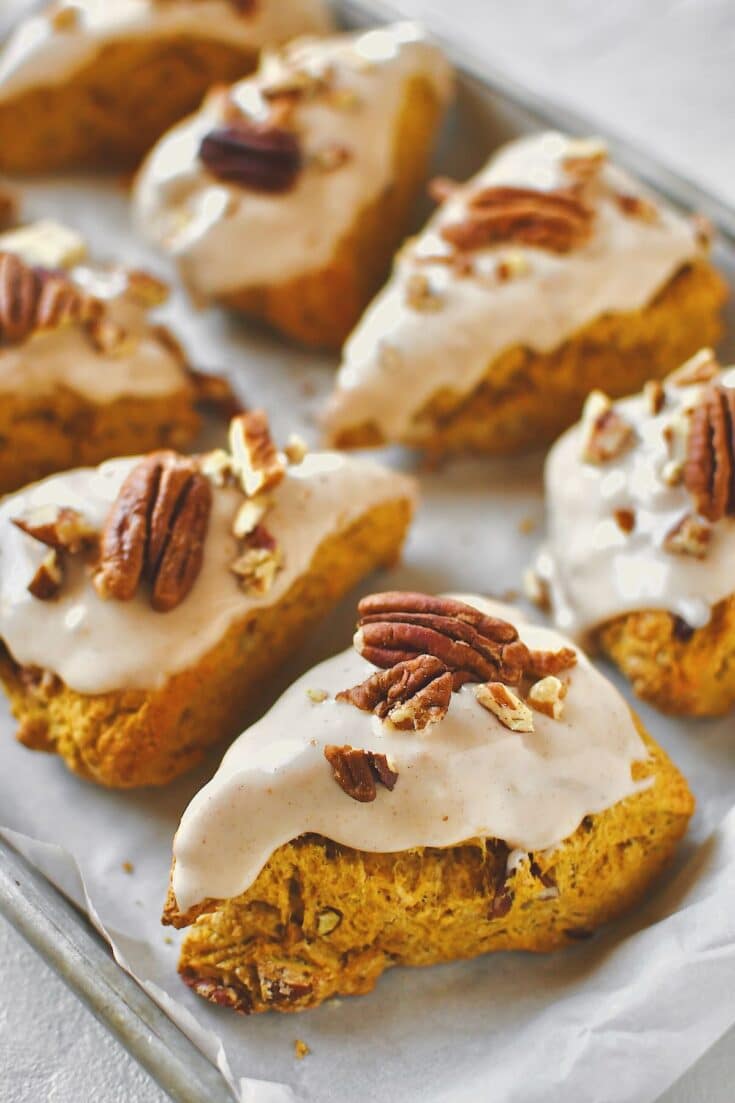 Pumpkin Scones, on a tray, topped with maple glaze and chopped pecans, ready to eat.