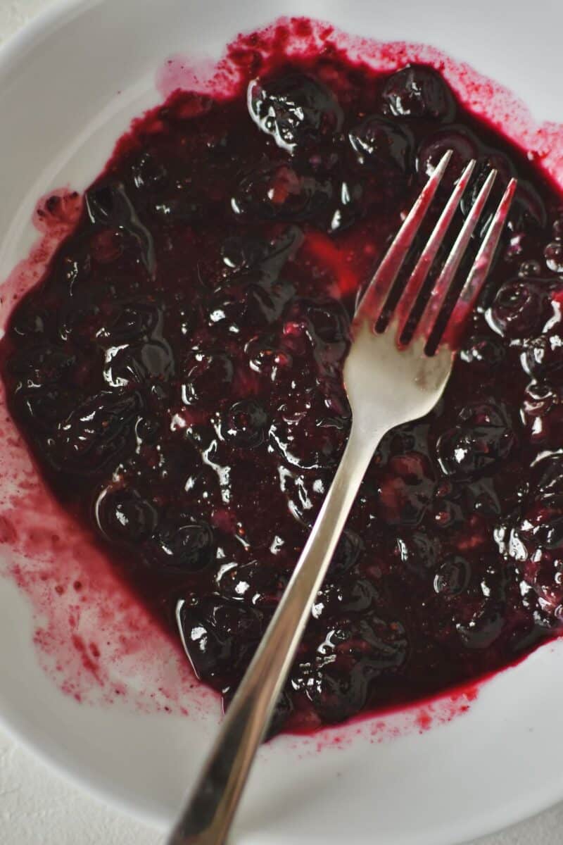 Mashing blueberries with a fork till they are soft and the juices have released.