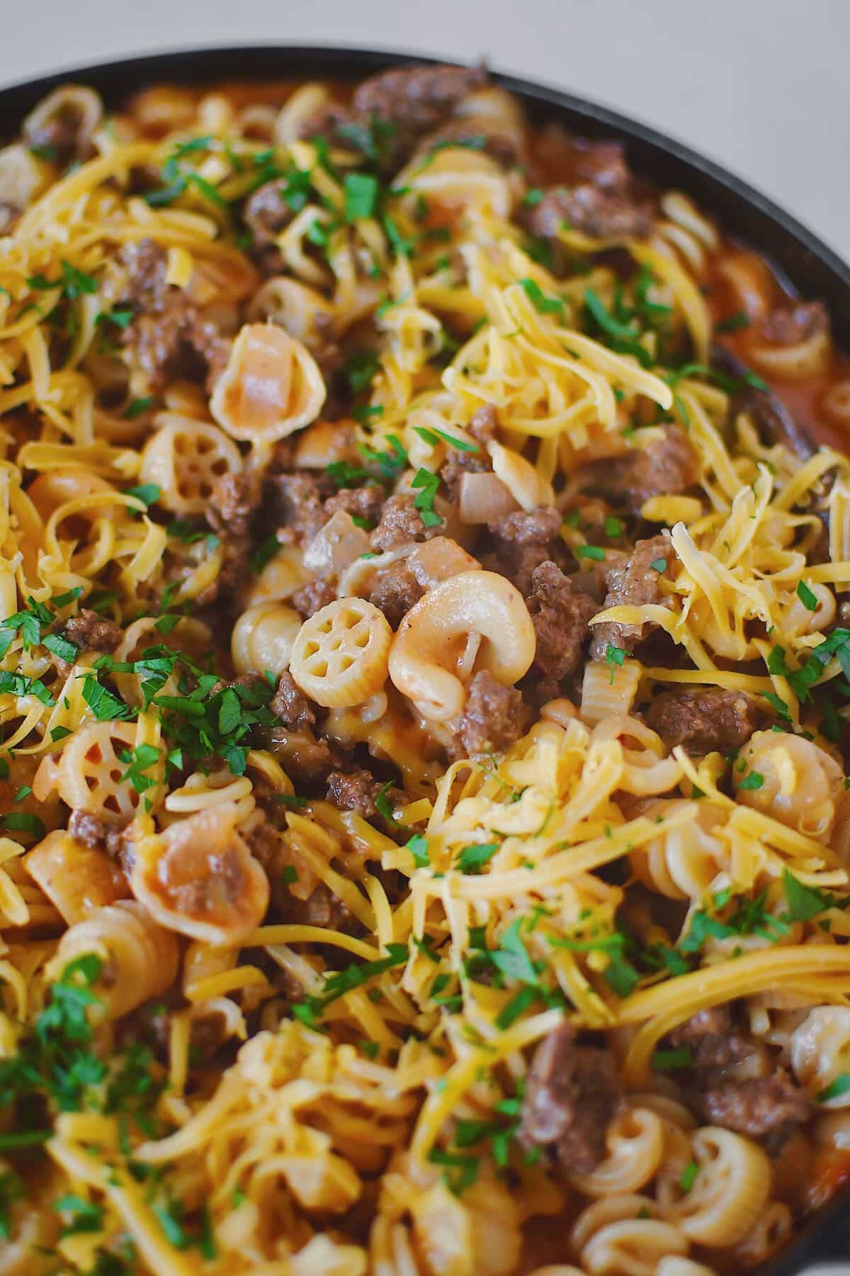 Finished Homemade Hamburger Helper in the pan, topped with cheddar cheese and parsley, ready to eat.