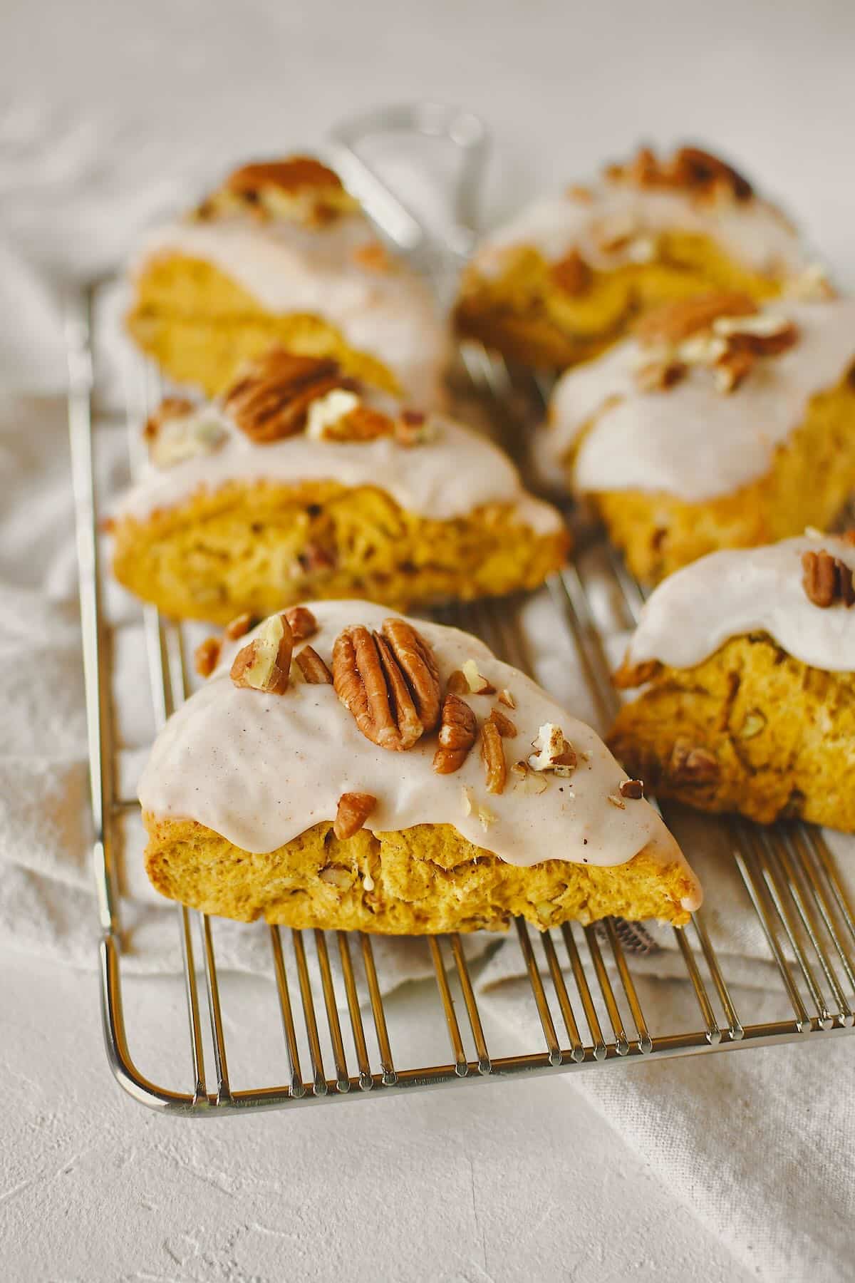 Pumpkin Scones, on a cooling rack, topped with maple glaze and chopped pecans, ready to eat.