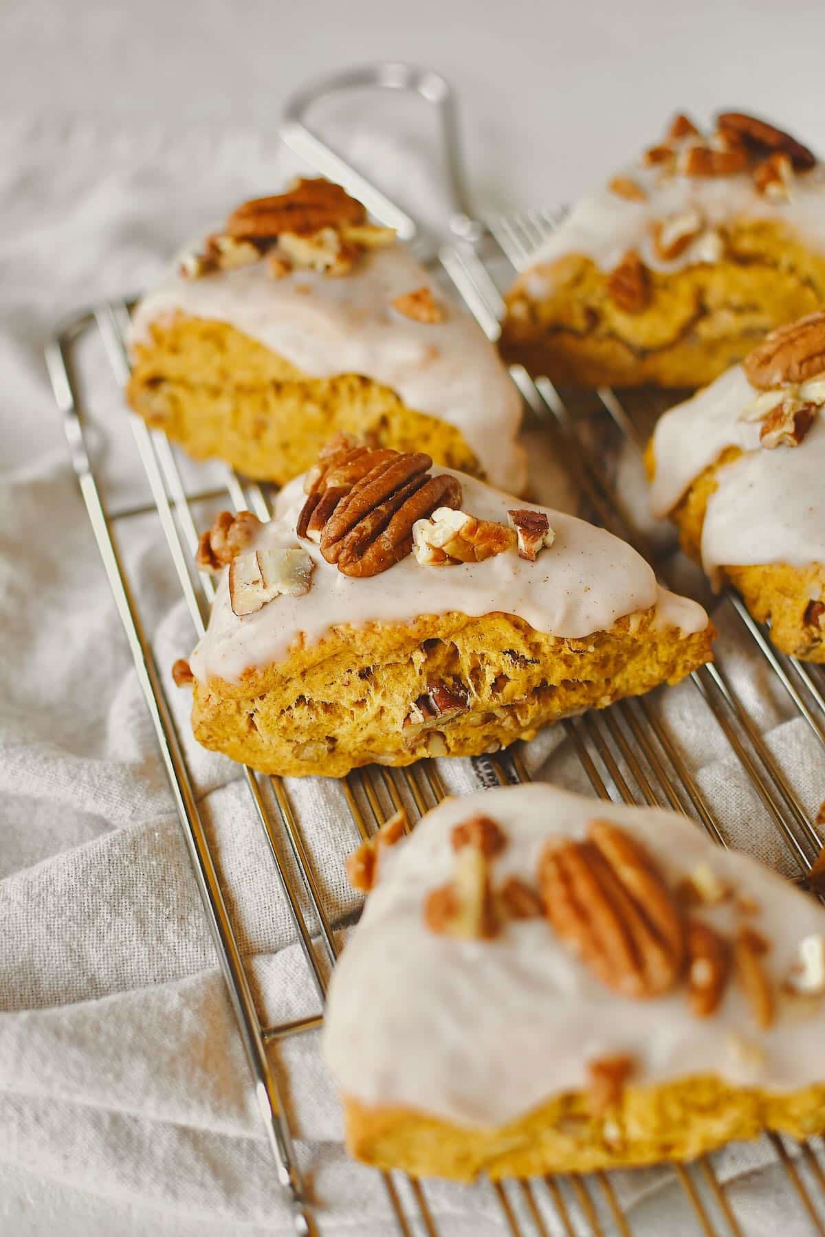 Pumpkin Scones, on a cooling rack, topped with maple glaze and chopped pecans, ready to eat.