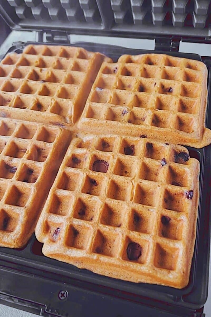 Waffles cooking on a large 4 square waffle iron.