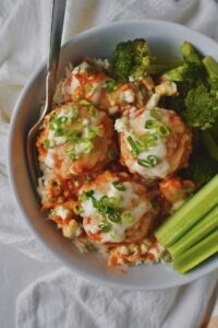 Looking down at Buffalo Chicken Meatballs served in a bowl over ranch rice with a side of roasted broccoli and celery.