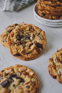 Looking at a slew of Coconut Pecan Chocolate Chip Cookies, on a table, ready to be eaten.