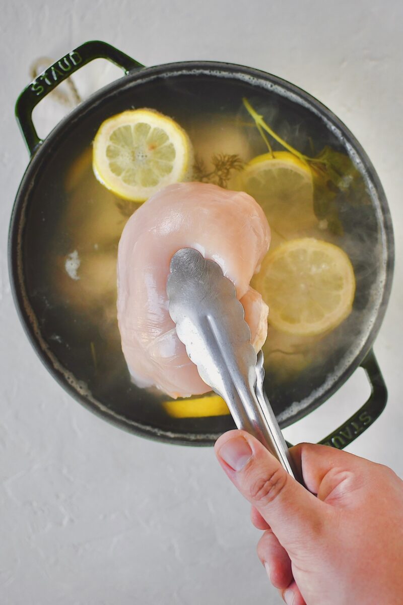 Dropping raw chicken breasts into the hot poaching liquid.