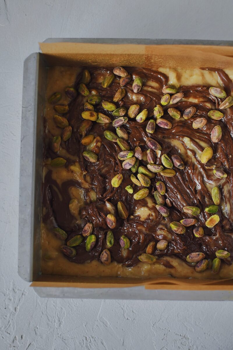 Batter placed in the prepared baking pan, topped with nutella that has been swirled in and topped with pistachios.