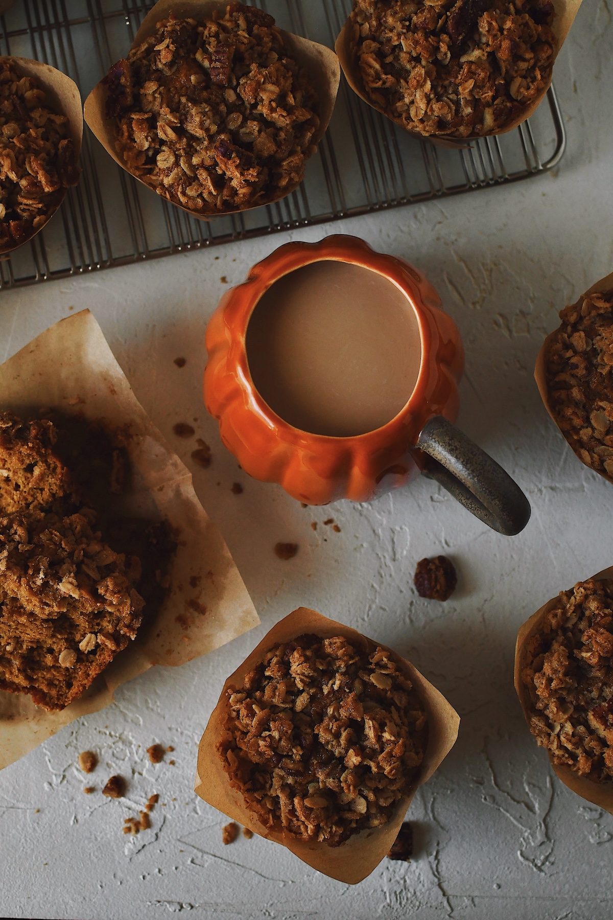 Looking down at a group of pumpkin banana muffins, one split open and a pumpkin coffee cup in the middle.