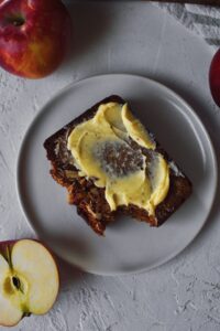 Looking Down at a slice of Apple Bread that has a bite taken from it and butter spread over the top.
