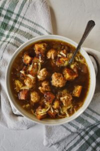 Looking down into a bowl of Cheesy French Onion Soup - Kendell's Version, filled with mini chicken meatballs, and gruyere croutons.