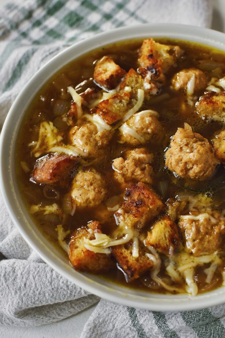 Looking into a bowl of Cheesy French Onion Soup topped with Gruyere Croutons and filled with Mini Chicken Meatballs.