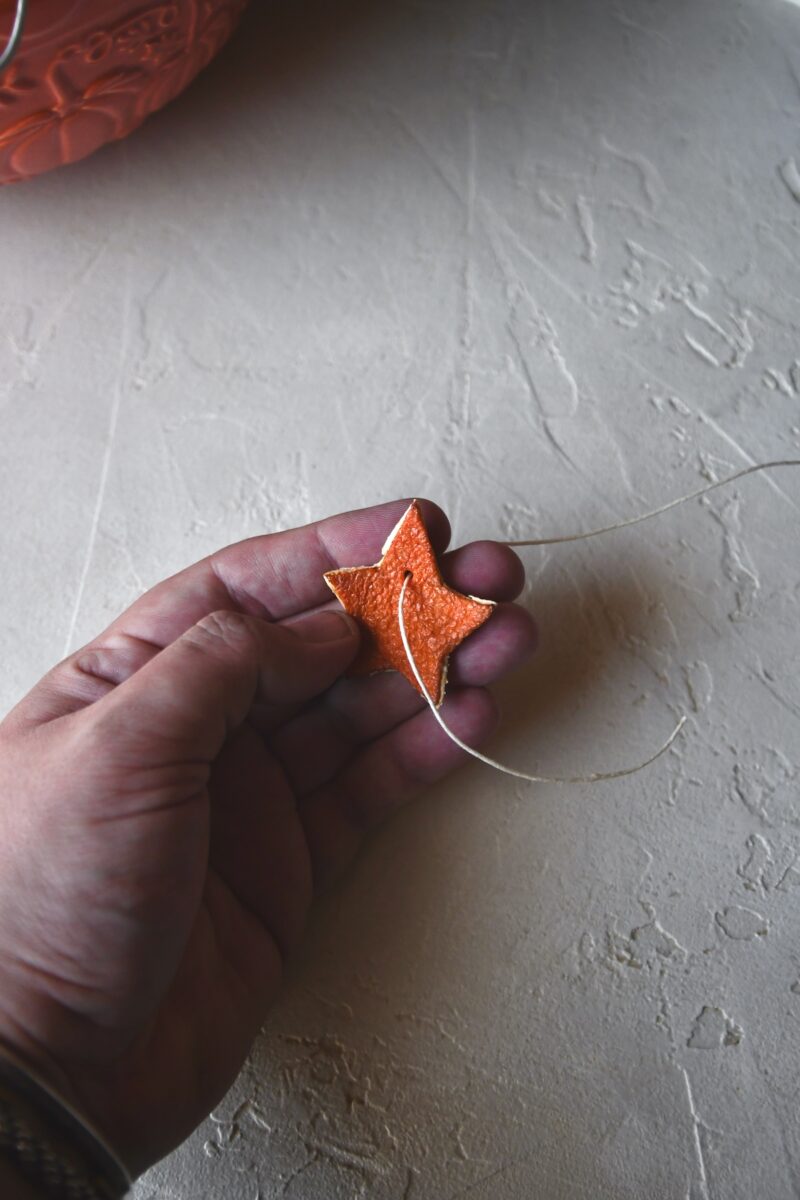 Poking the twine through a hole in dried orange peel stars.