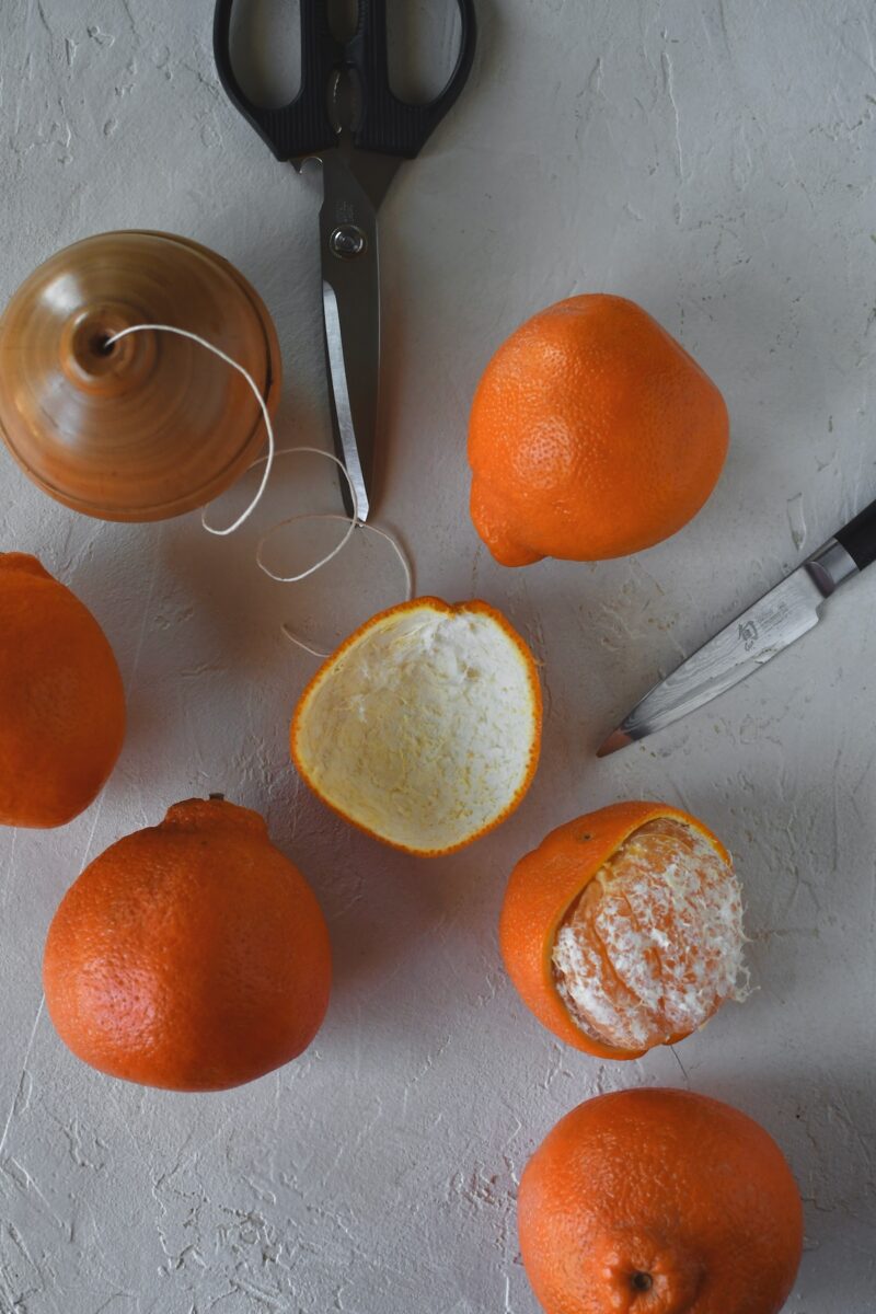 Oranges on a table, one has had its peel removed in one large piece.