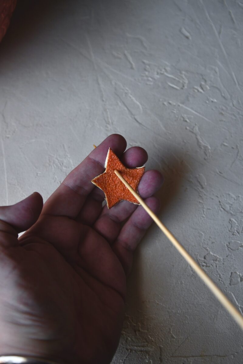 Using a skewer to poke a hole in dried orange peel stars.