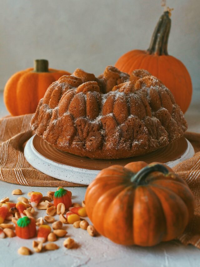 Whole Pumpkin Donut Bundt Cake on a tray surrounded by pumpkins and candy corn and peanuts.