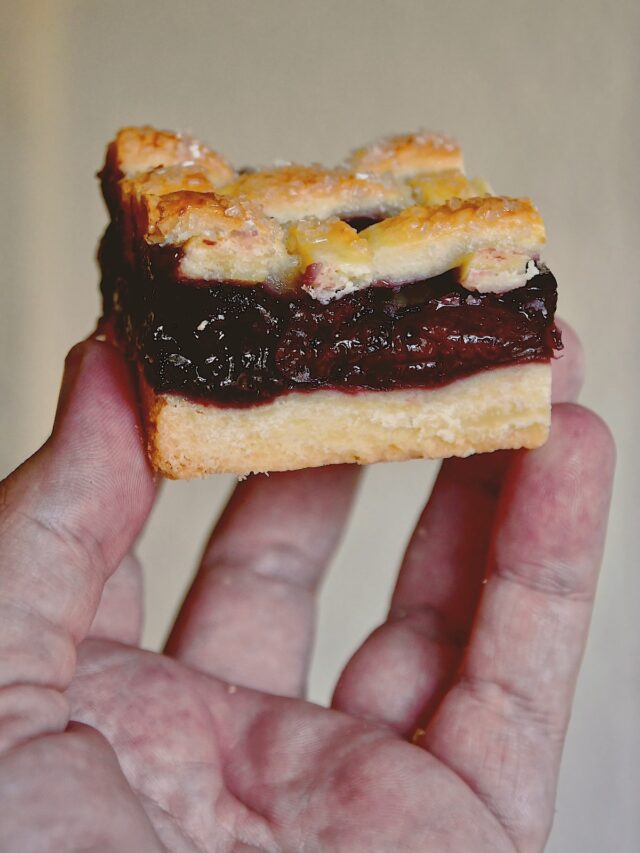 Holding up a cherry pie bar so you can see all the layers and the flakey shortbread base and flakey lattice pie crust top.