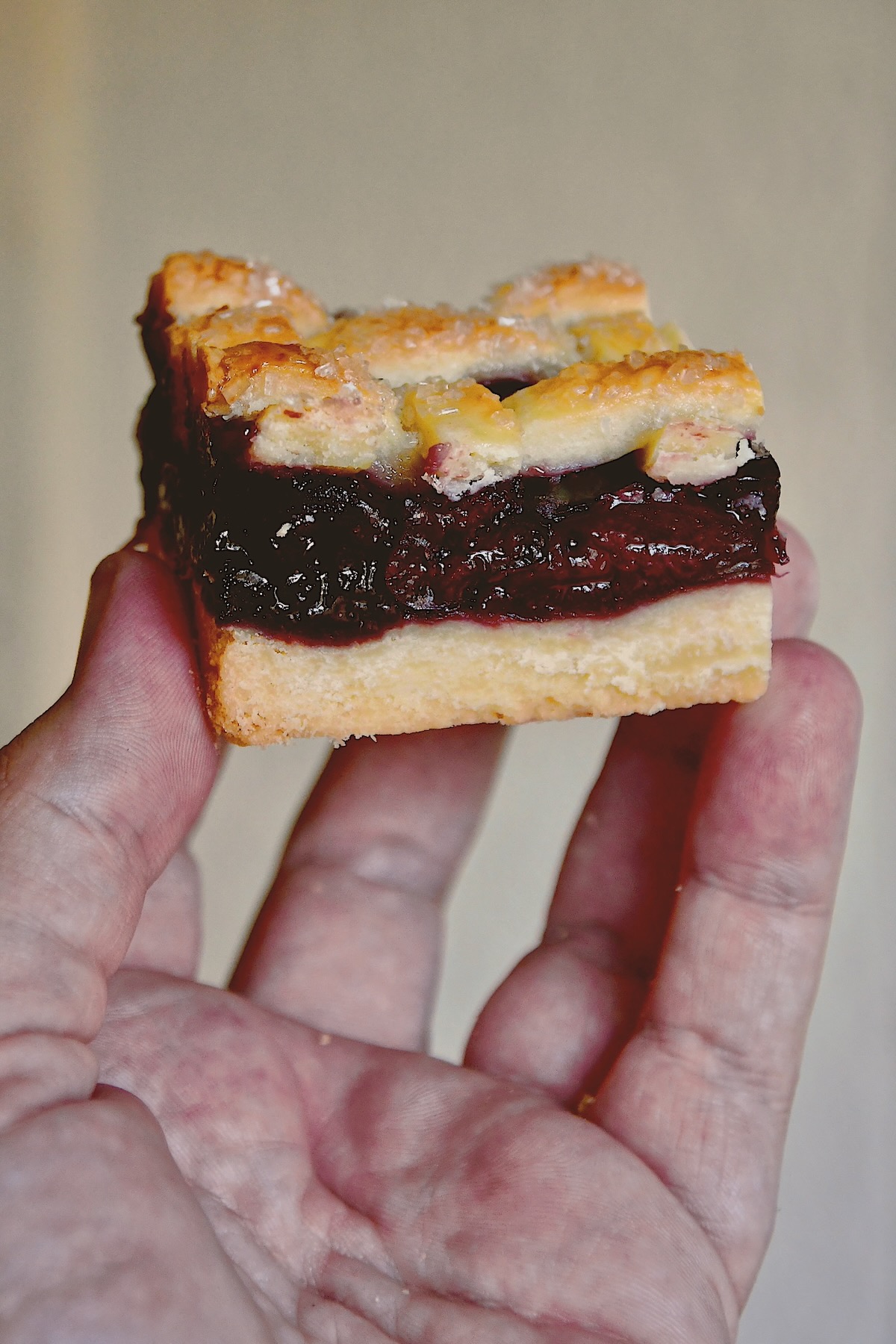 Holding up a cherry pie bar so you can see all the layers and the flakey shortbread base and flakey lattice pie crust top.