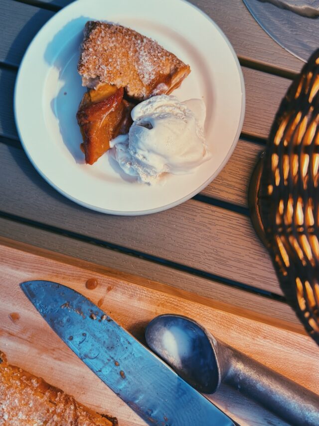 Peach Galette cut in a board and a slice on a plate with a side of ice cream on the back patio on a summer night!