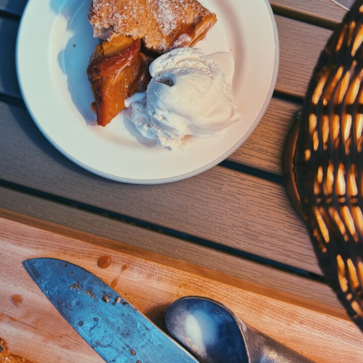 Peach Galette cut in a board and a slice on a plate with a side of ice cream on the back patio on a summer night!